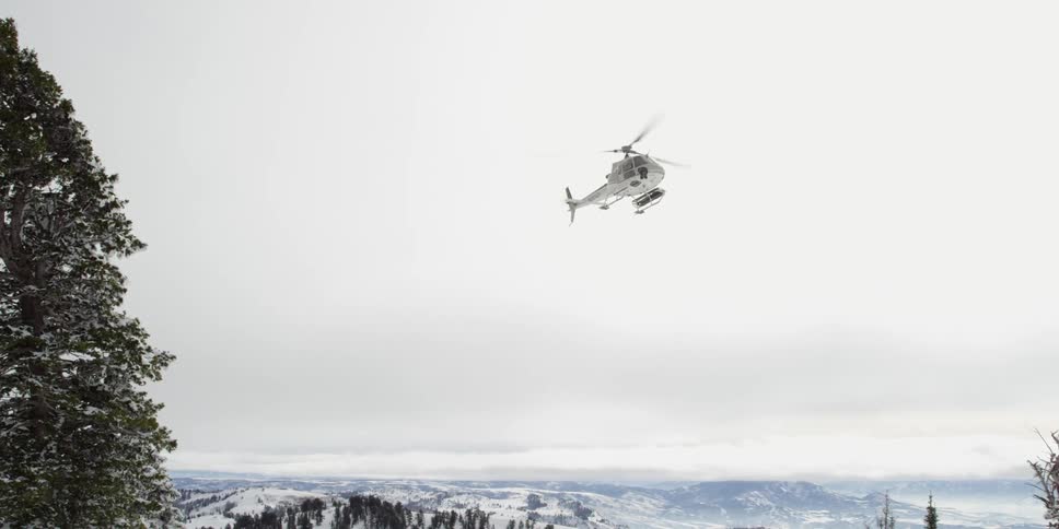 A helicopter flies over snow covered mountains
