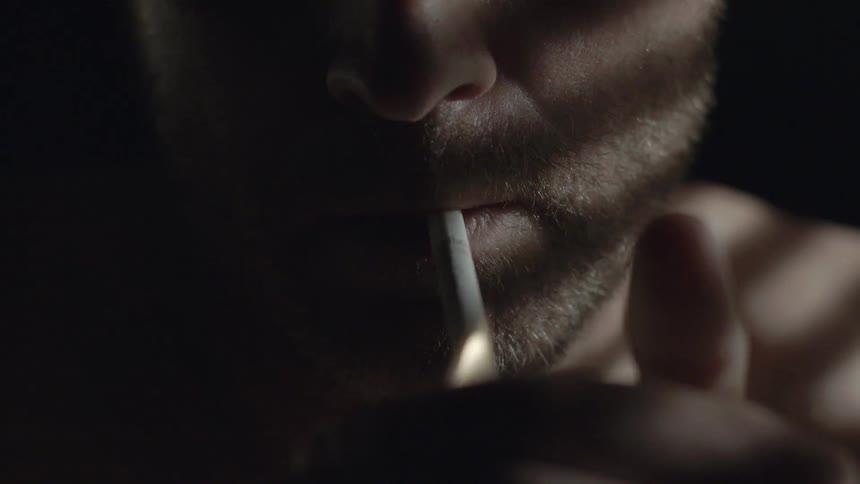 A man lights a cigarette in a dark room