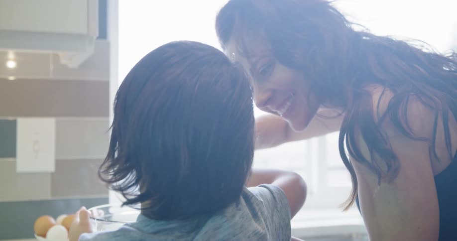 A woman helps her son stir a bowl of food in their kitchen