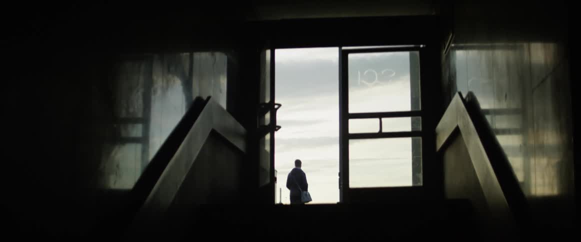 A person stands outside a building as cars drive by
