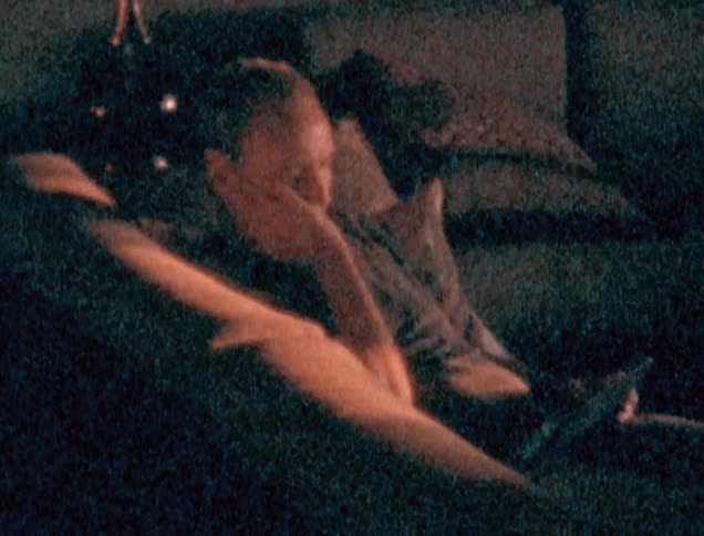 A man is laying on the couch reading his tablet