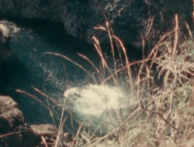 A girl in shorts and a tee shirt jumps off a rocky ledge and splashes into the water below
