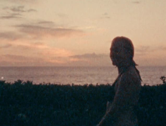 People walk past a woman watching the ocean