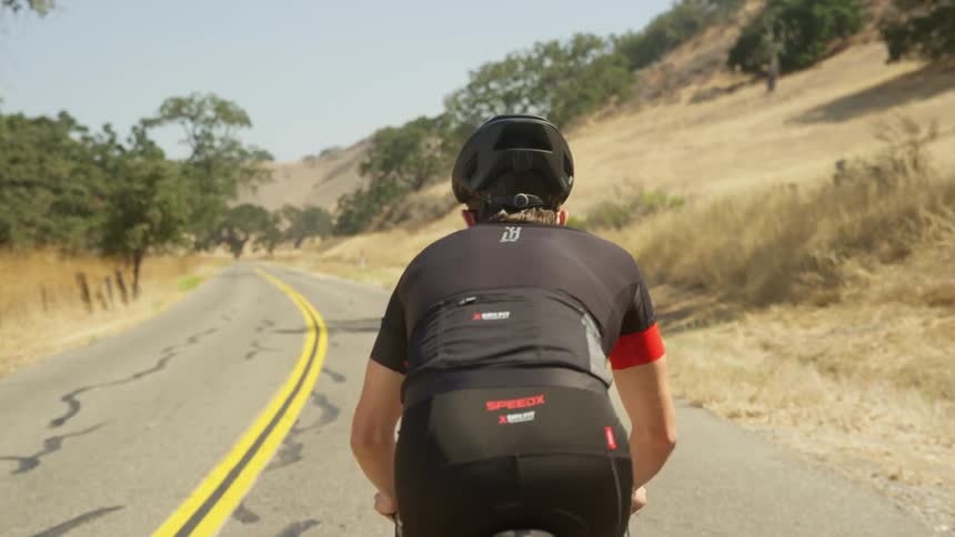 Male cyclist with black mtb helmet and cycling jersey rides a bicycle on a highway next to a mountain