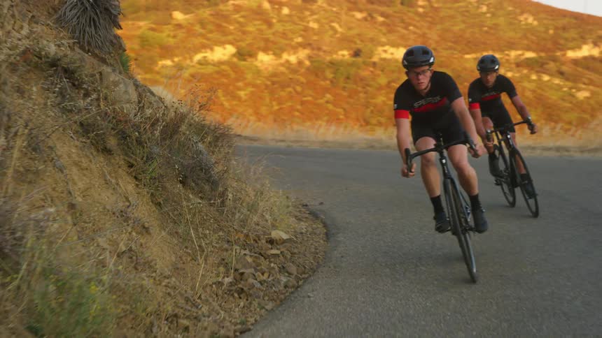 Two bike riders take a curve on a mountain road