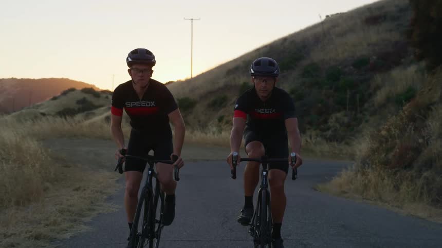 Two bicyclists ride down a road in a rural area