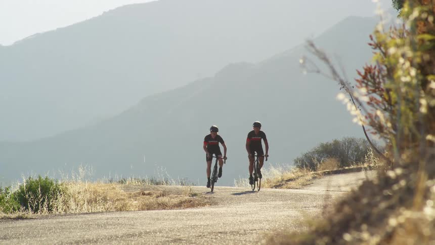 Two determined cyclist ride bikes on a mountain road with mountains in the background