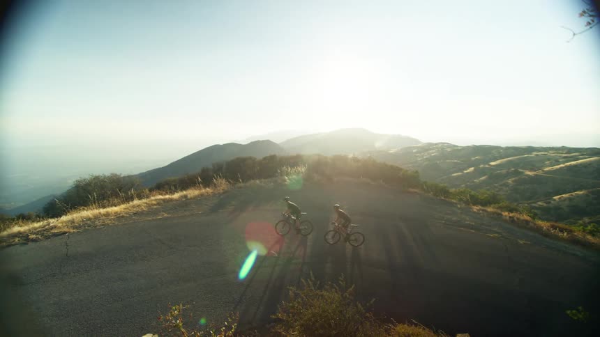 Two bicyclists ride up a hill on a road outdoors