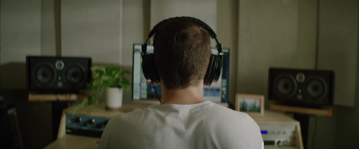 A man with headphones sitting in front of a computer and speakers
