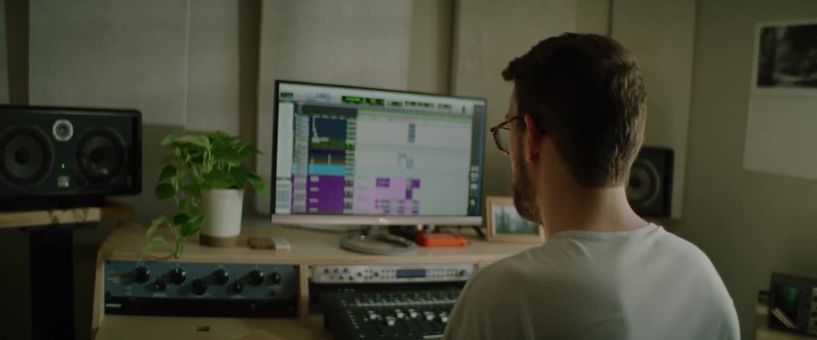 A young white man sits at a computer and messes around with a soundboard
