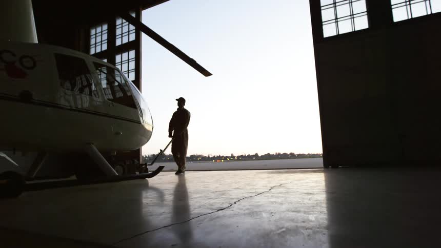 Man pulls an helicopter from a hangar into an airfield