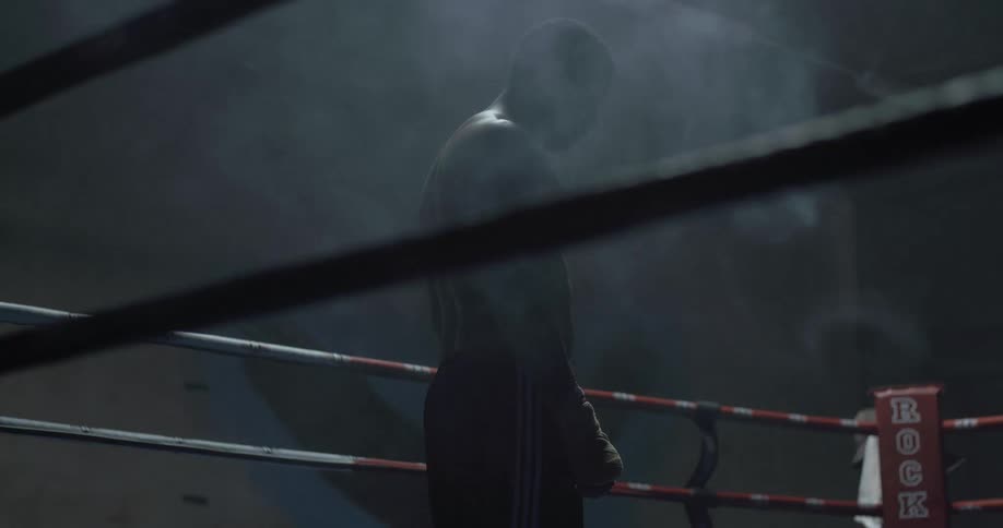 A boxer is standing in a dark ring