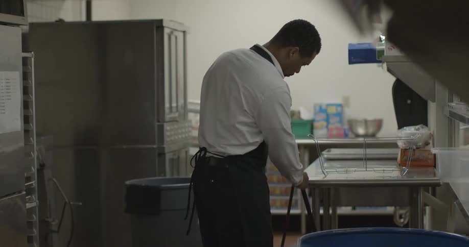 A man sweeps the floor of a commercial kitchen