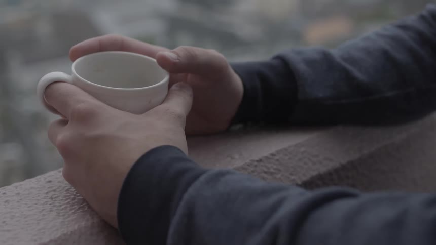 A person is looking over a balcony while holding a mug