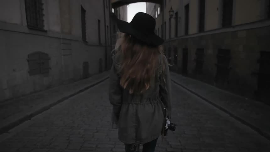 A woman holding a camera is walking down an alley
