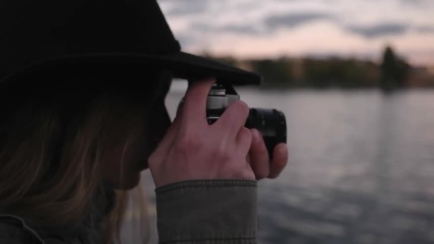 A woman in a cowboy hat photographs near a lake