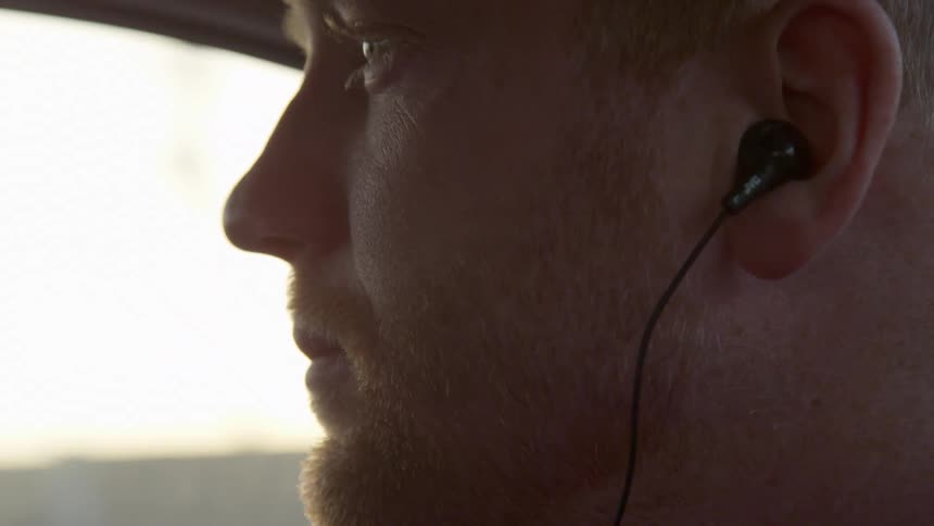 Redhead sits in vehicle wearing earphones while scenic view passes by outside