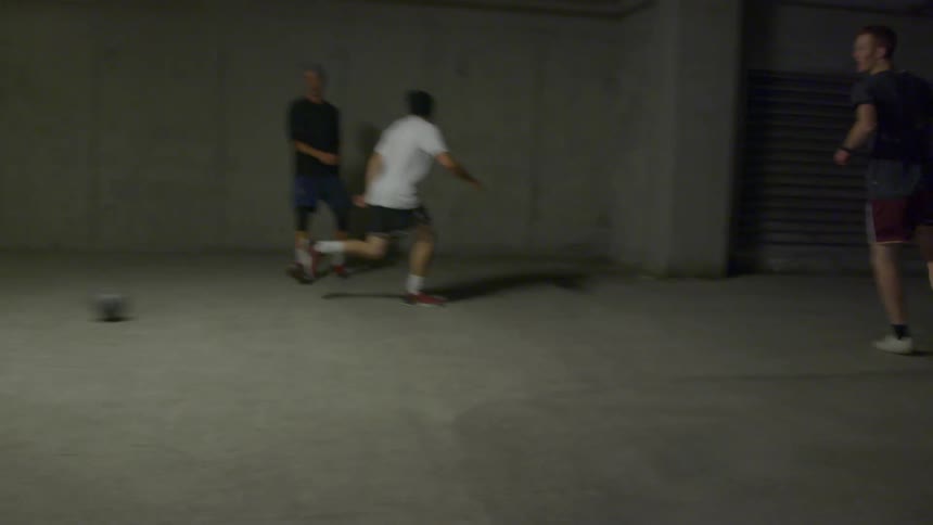 A group plays soccer inside a parking garage