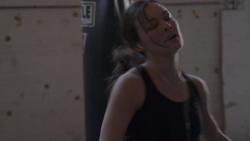 Woman aggressively punches a punching bag then kicks it while in a gym