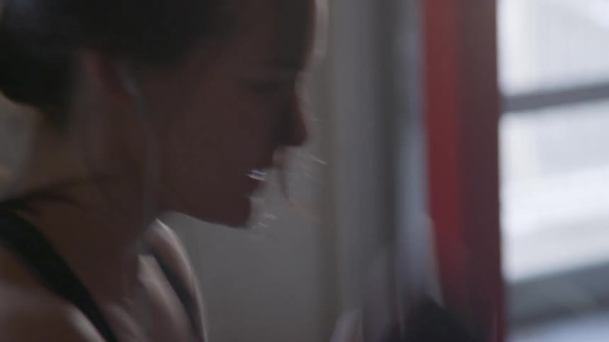 A white woman hits a punching bag in a gym
