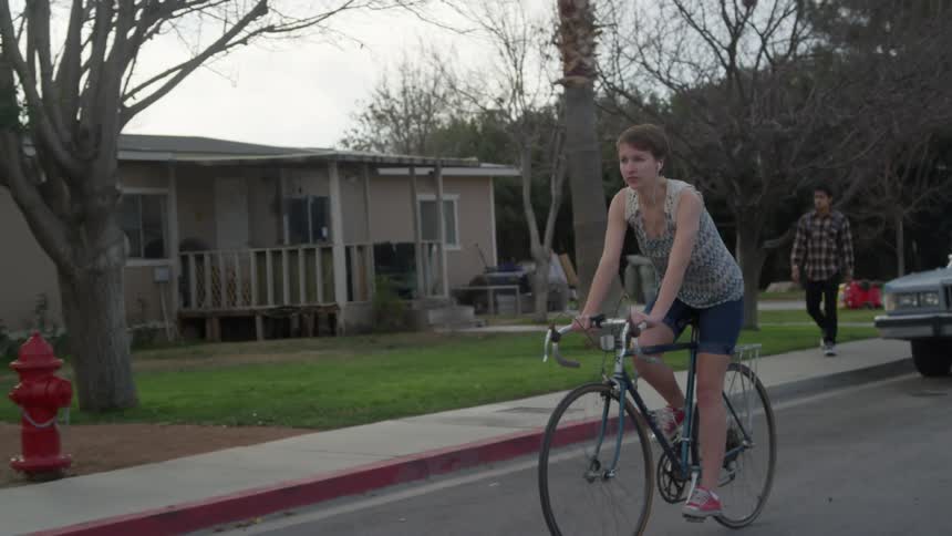 A teenager bikes down a neighborhood street as a boy walks along