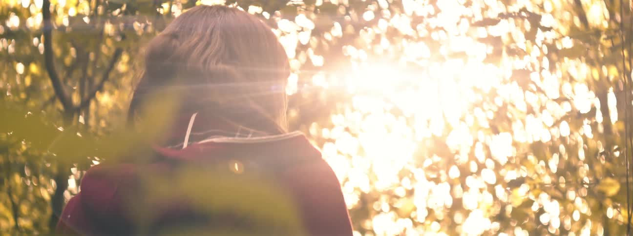 Woman wearing hoodie stands under trees looking around