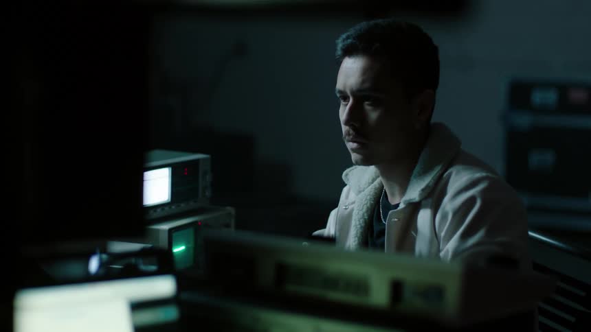 A man sits surrounded by a variety of electronic equipment