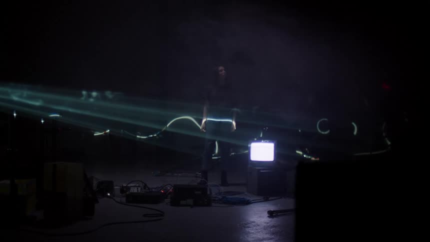 A white woman walks around a television set and various machines