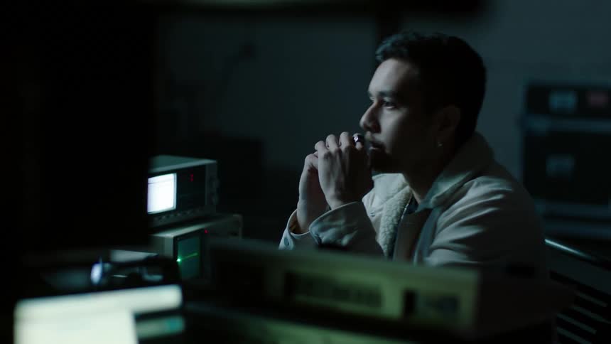 A man sits at a desk and looks at monitors
