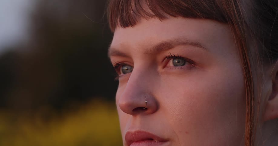 A womans face as she stares into the distance while outside in a wooded area at dusk