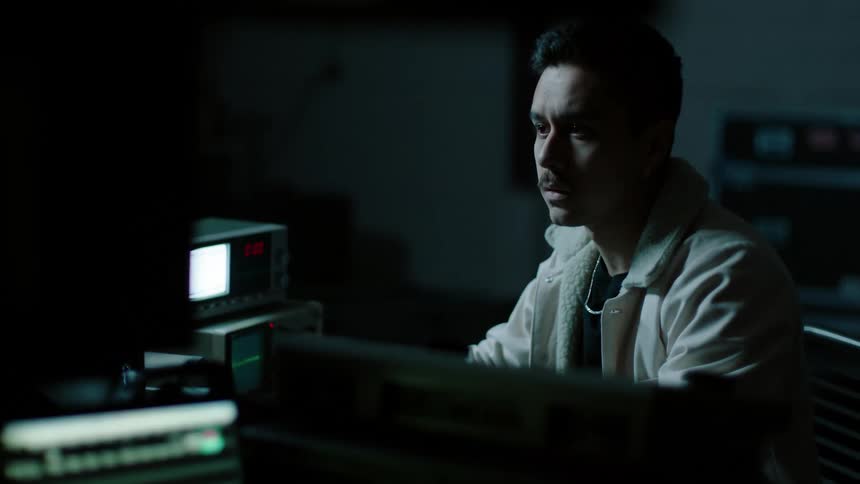 A man sitting on a chair in front of a computer surrounded by equipment
