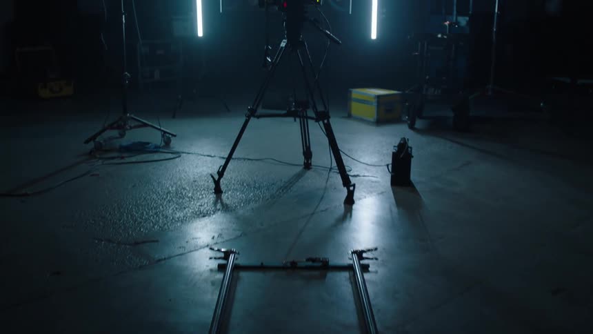 Video camera on a tripod stands at the end of a track in a dark room