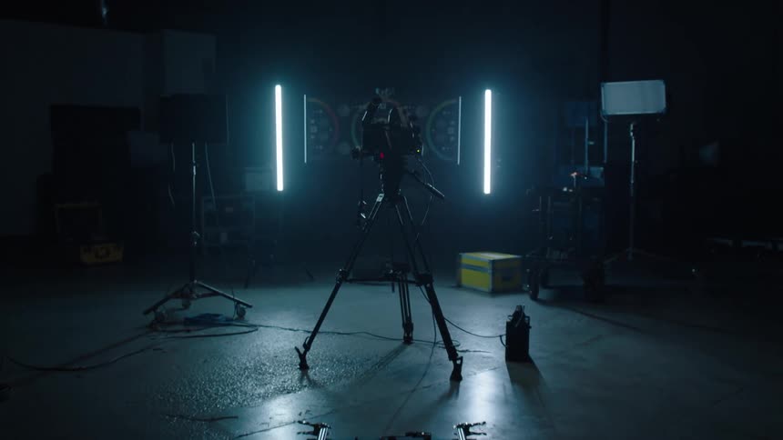 A camera sits on a tripod in a dark and empty studio