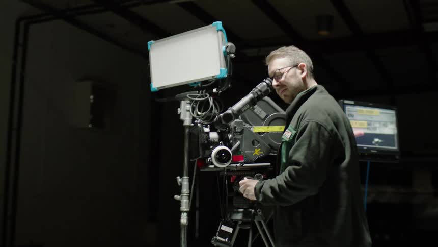 A man in a studio filming on a camera with a monitor in the background
