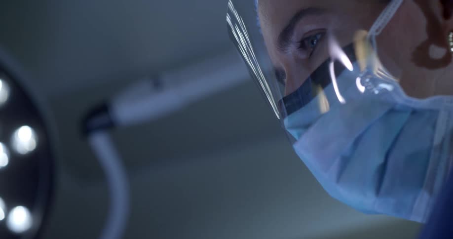 A female surgeon in personal protective equipment working under surgical lighting
