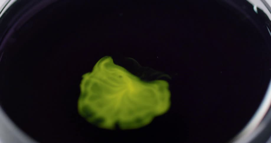 A yellow dye is dropped into a can of water and begins to spread and mix with the water