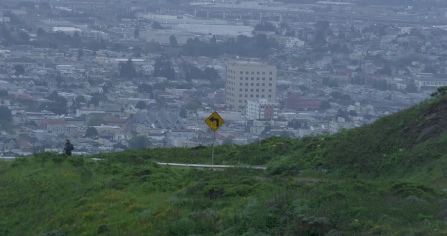 A jogger runs on a road on a hill overlooking the city and neighborhood below
