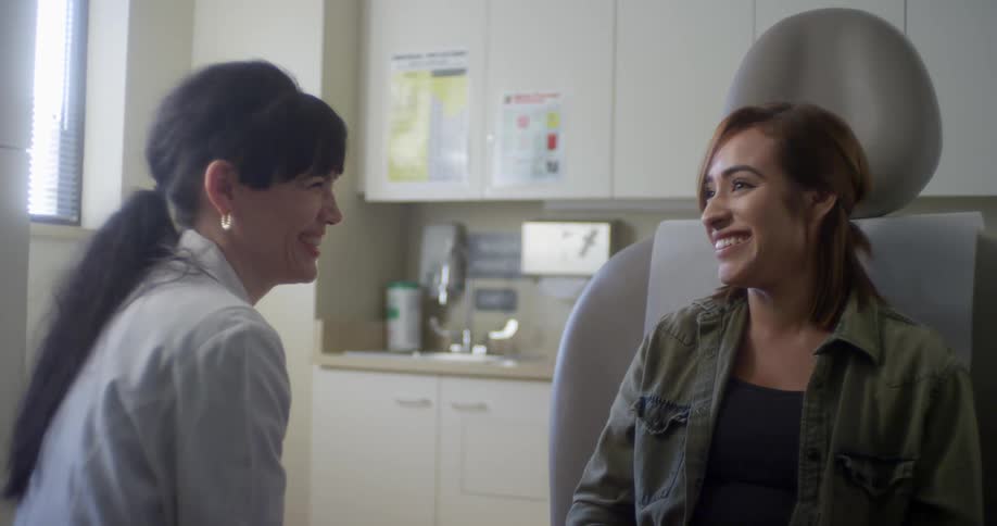 Female dentist with white lab coat talks a patient sittng an in dental chair in dentists office