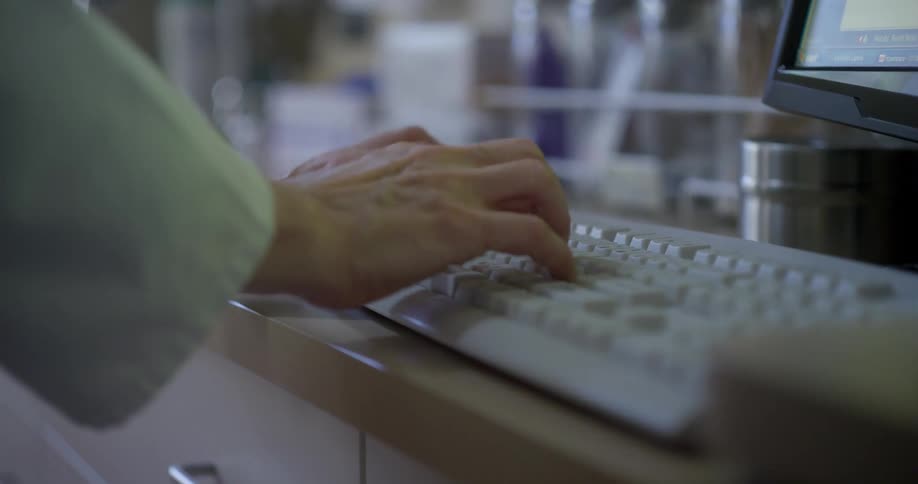 Woman wearing white coat stands while entering data on keyboard