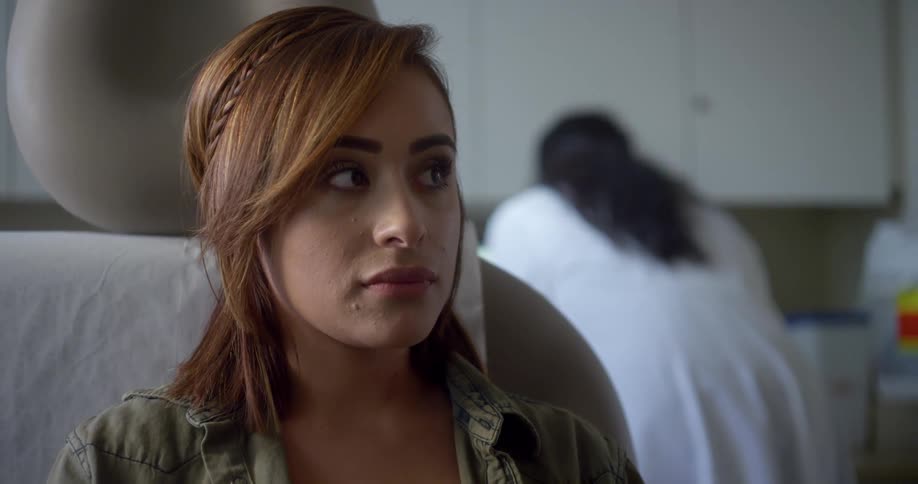 A hispanic woman looks sad sitting in a chair at a doctors office