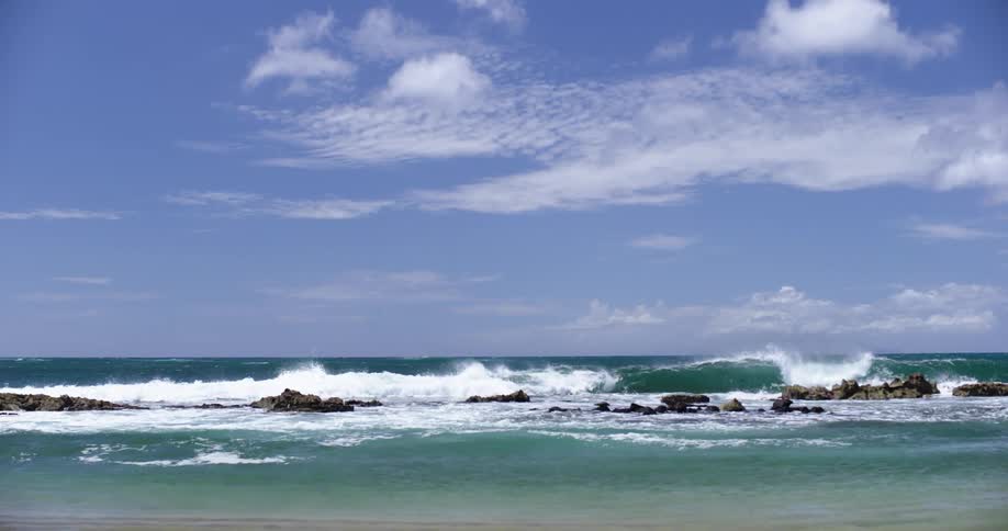 Ocean waves roll into a beach and crest and break on a line of rocks