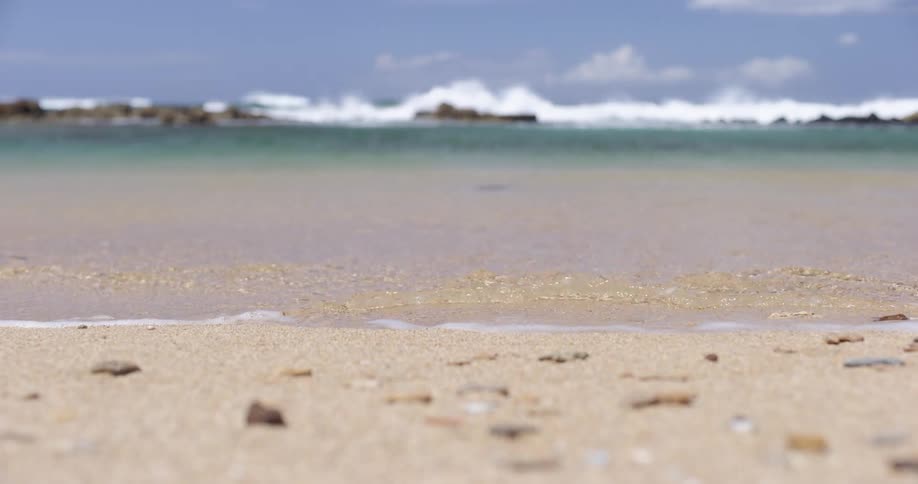 A ground level view of sand on a beach with crashing waves in the background