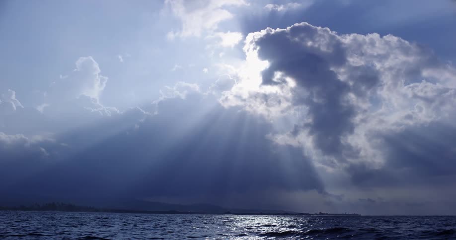 The sun hides behind dense clouds in a sky over the ocean