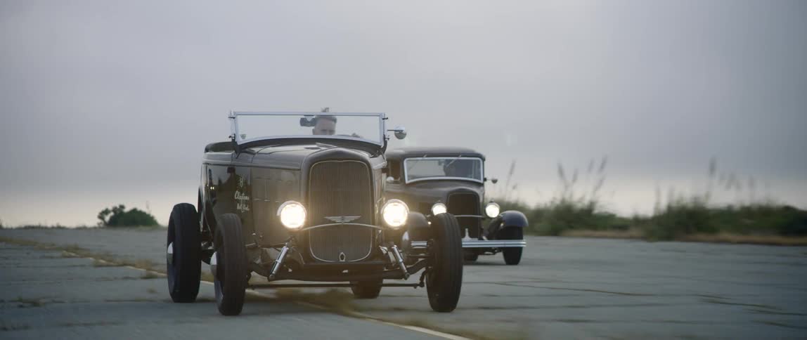 Two men race classic cars in a parking lot
