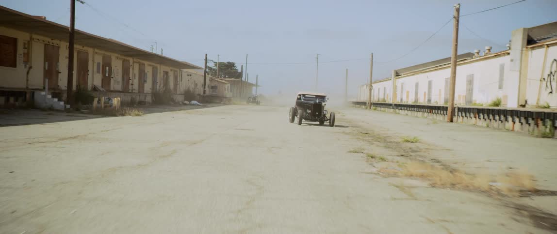 A driver drives a classic car wildly through a parking lot and past a row of motels