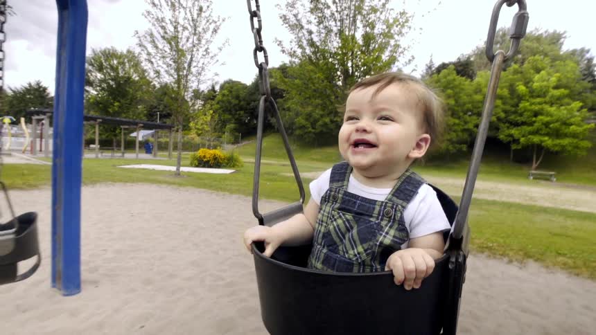 A laughing toddler enjoys a swing at a playground with her father