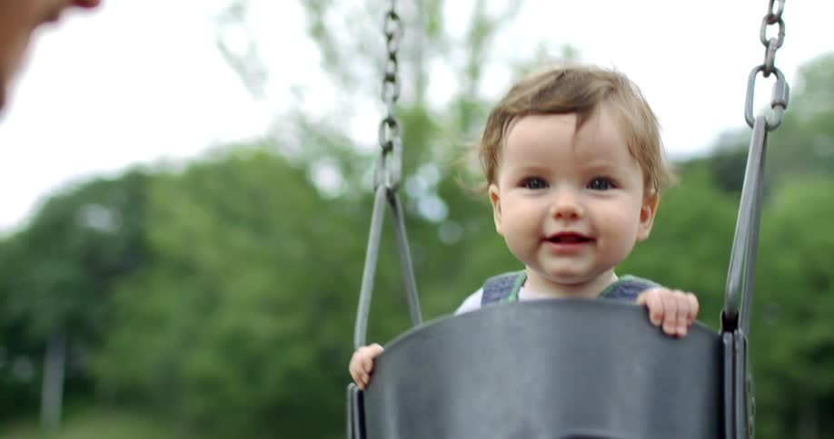 Happy baby swinging in a bucket swing at the playground