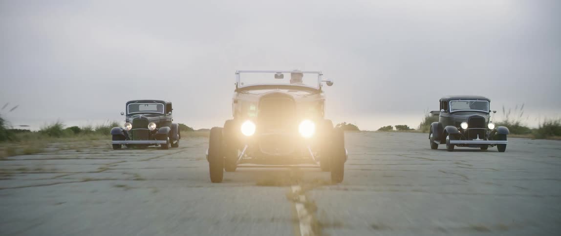 A trio of vintage vehicles travel down an old dilapidated road in formation