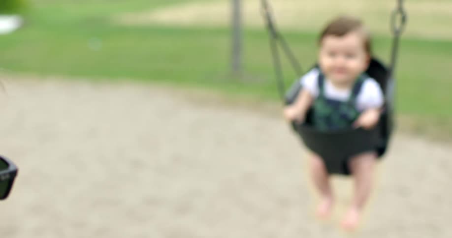 Baby being pushed on bucket swing by dad at a playground