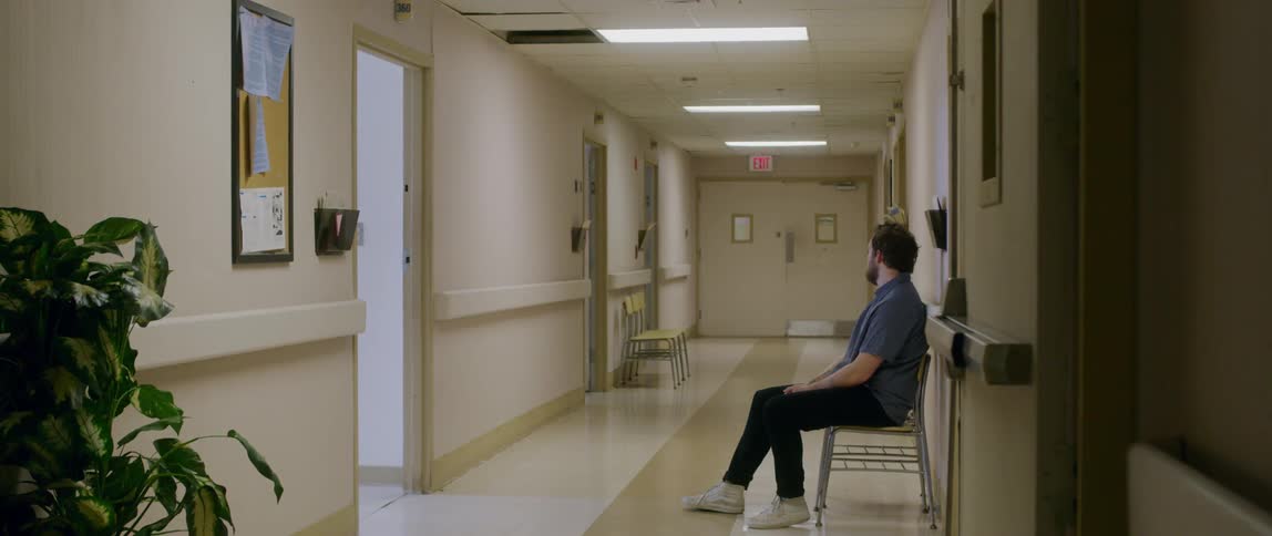 A white man sits in a chair in a hallway at a hospital